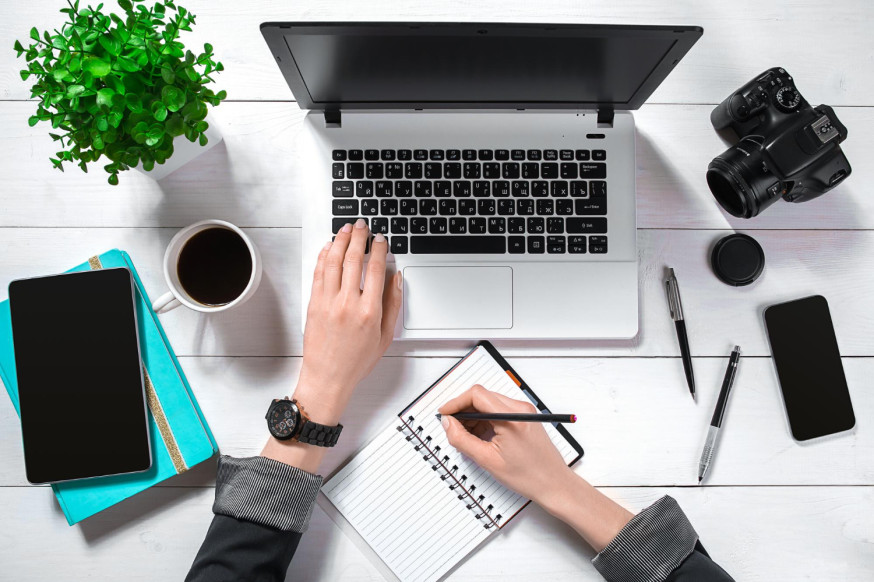 Afbeelding: Flat lay van een werkplek van een fotograaf met laptop, camera en notitieboek voor het maken van een strategisch ondernemingsplan
