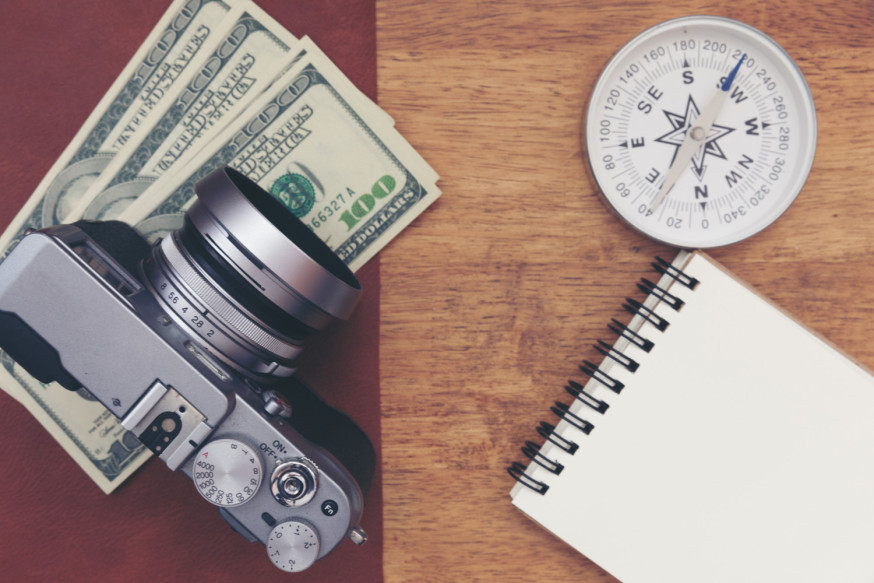 Afbeelding: Een camera, kompas en contant geld op een houten bureau als symbool voor de financiële koers van een fotografiebedrijf