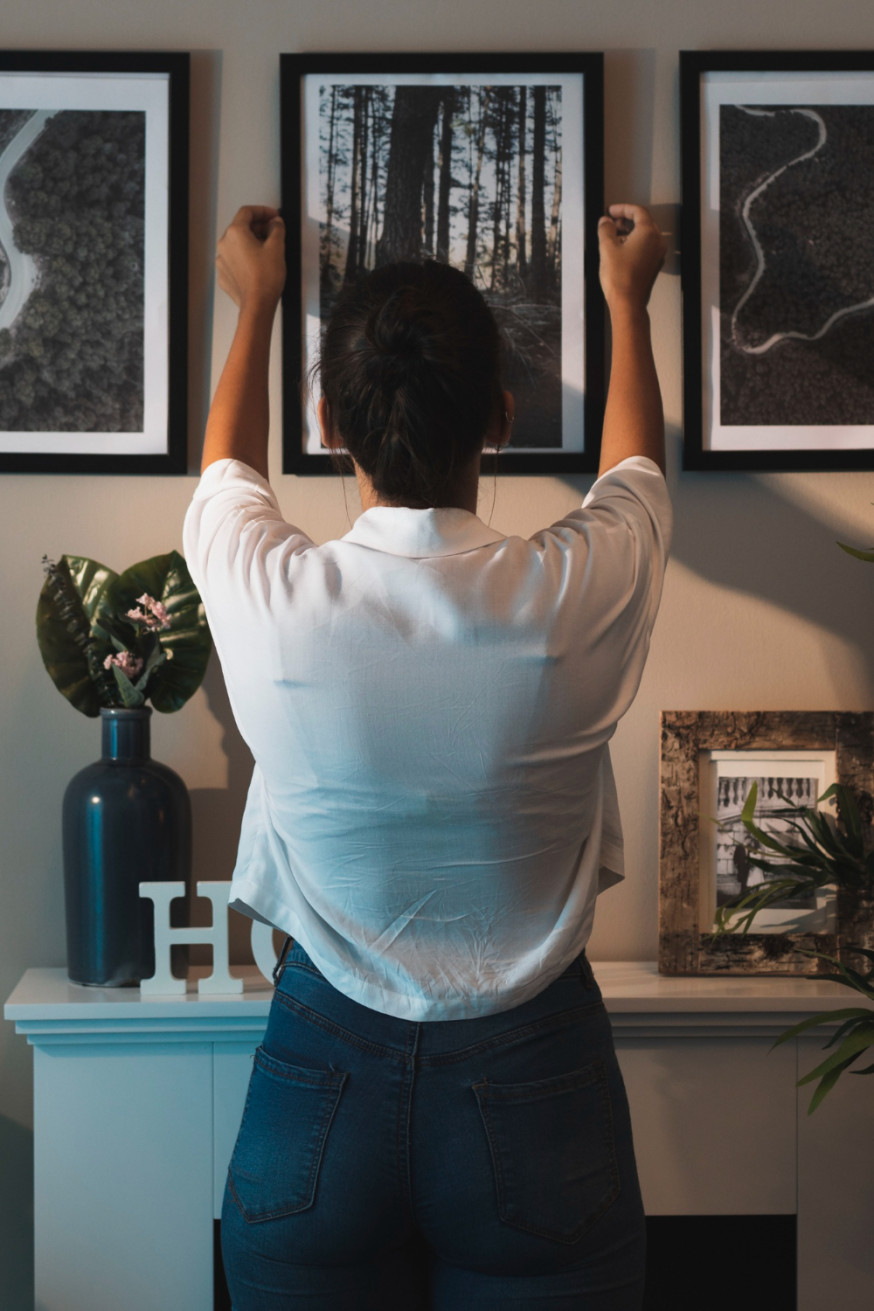 Afbeelding: Een fotograaf hangt een grote ingelijste zwart-wit foto aan een muur ter illustratie van de fysieke manifestatie