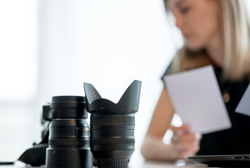 Afbeelding: Close-up van professionele camera-objectieven en een fotograaf die investeringsplannen doorneemt op de achtergrond