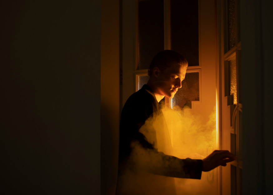 Afbeelding: Mysterieuze foto van een man bij een glazen deur met cinematografisch oranje tegenlicht en rook voor storytelling