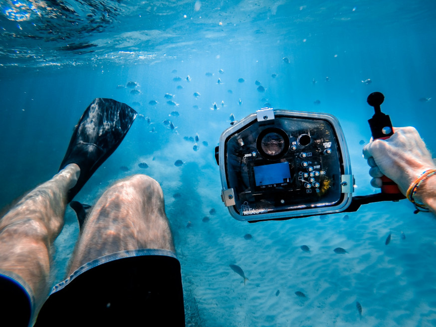 Point-of-view (POV) foto vanuit de ogen van een duiker die naar zijn eigen vinnen en een camera in onderwaterhuis kijkt in helder blauw water met vissen