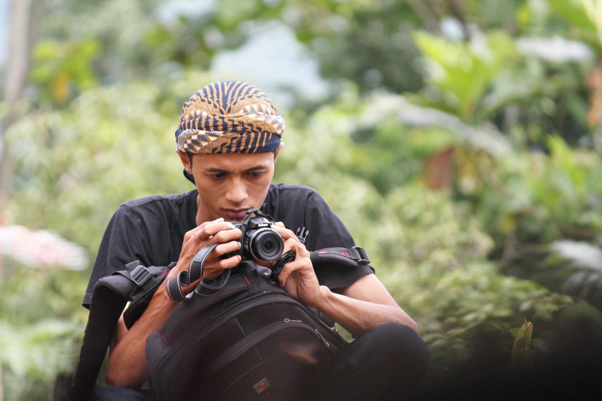 Afbeelding: Fotograaf kijkt geconcentreerd op het scherm van een oudere zwarte Nikon Coolpix camera, illustrerend voor de 'slow photography' mindset en de focus op compositie boven snelheid